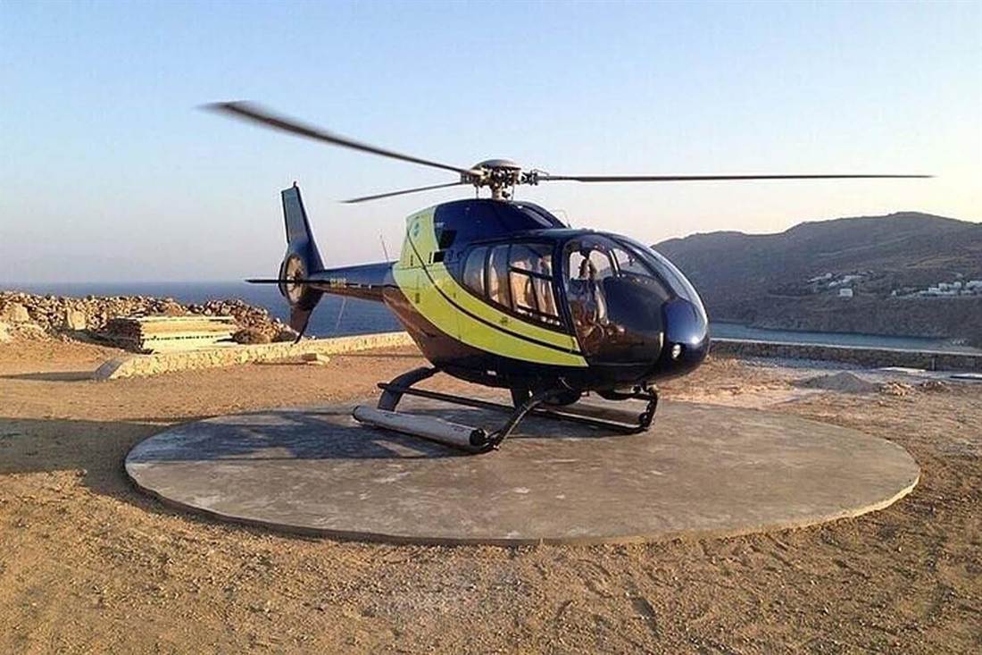 Dark blue and yellow helicopter parked on a round helipad above the sea on a Cyclades island at sunset
