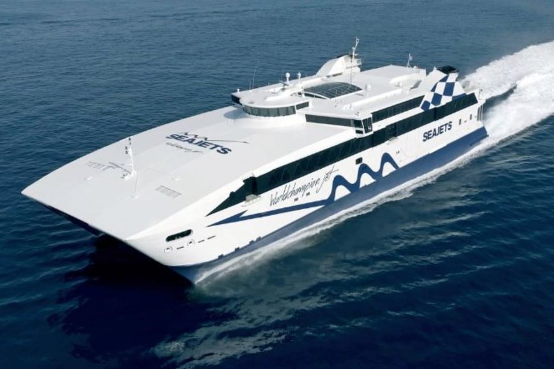 White and blue Seajets high-speed catamaran ferry racing across the deep blue Aegean Sea with a white wake