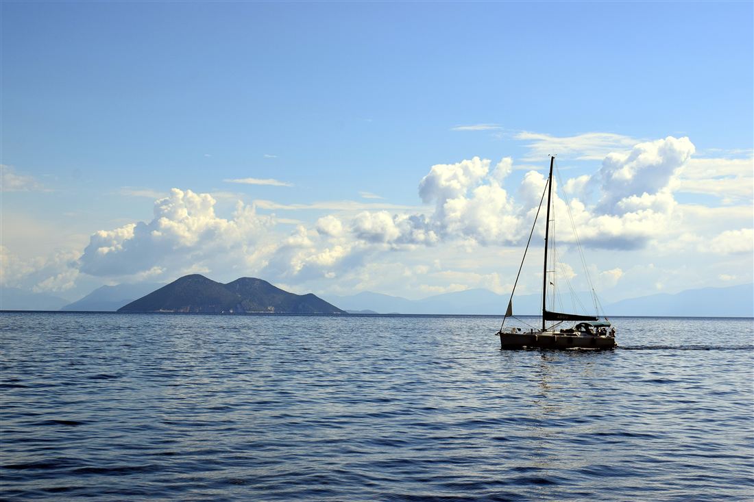 A sailing boat passing the green peaks of the islet of Atokos in the Ionian Sea, a stop on an Ithaca boat trip.