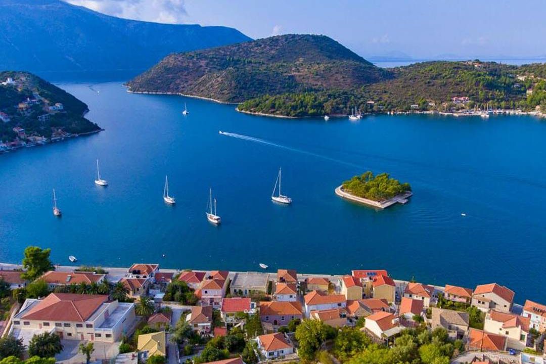 Aerial view of Vathy on Ithaca, with red-roofed houses, sailing boats and the small wooded Lazareto islet in the deep blue bay.