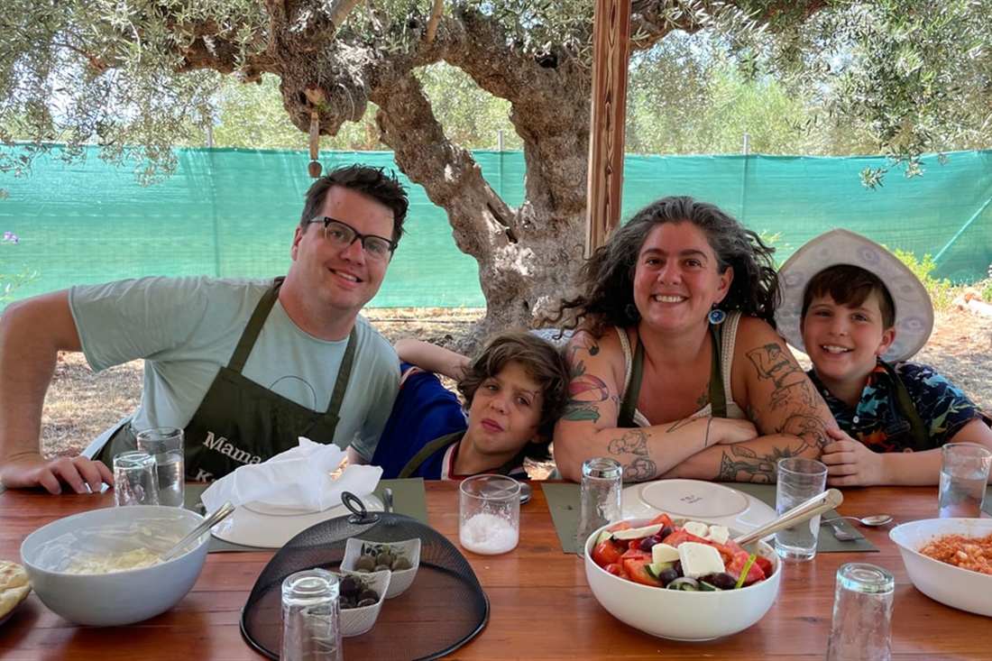 A family at a table of Greek dishes under olive trees at the end of a Kalamata cooking class.