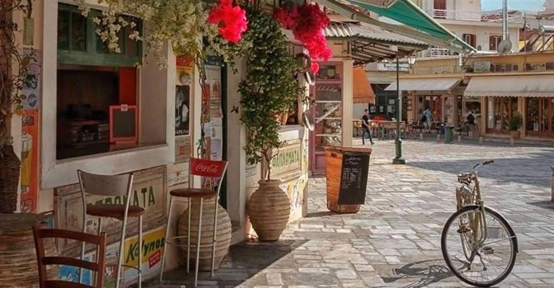A sunny square in the old town of Kalamata with a cafe, potted plants, red bougainvillea and a parked bicycle