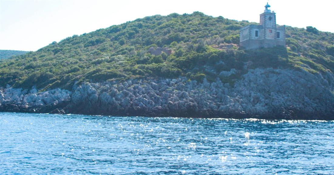 A green headland with a small stone lighthouse above clear water, seen from the boat on a Kalamata snorkeling trip.