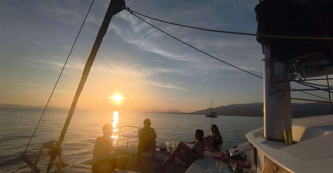Guests on the deck of a catamaran watching the sun set over the Messenian Gulf off Kalamata