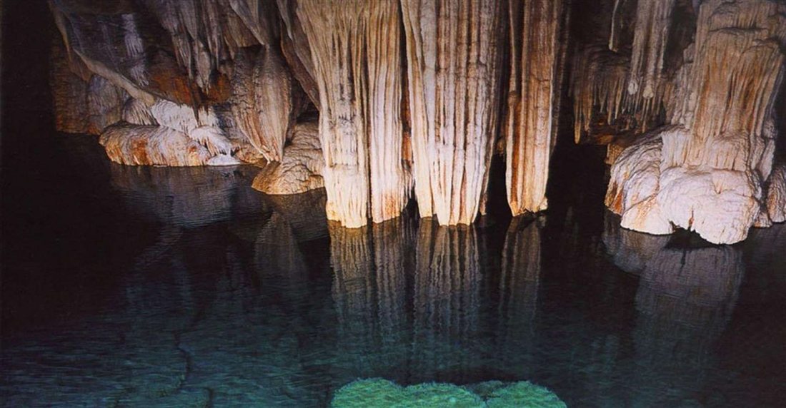 Stalactites hanging over the still water of an underground lake in the Cave of the Lakes