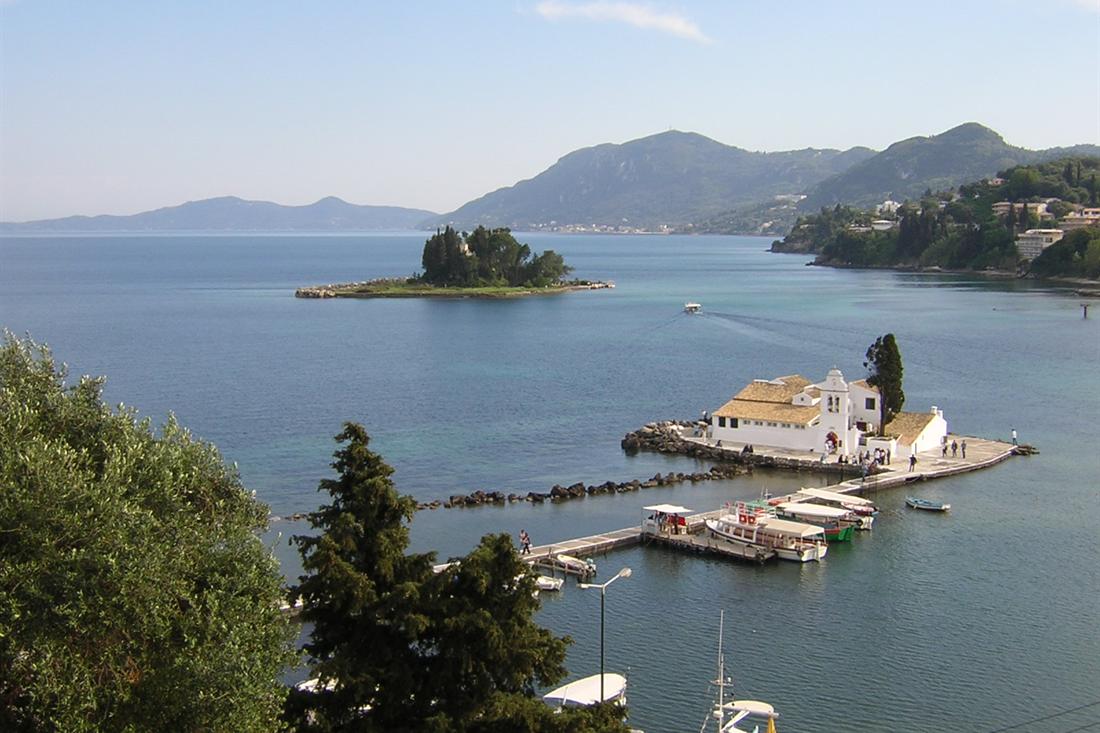 Vlacherna Monastery on its causeway and Mouse Island across the bay, seen from the Kanoni hillside past olive and pine trees
