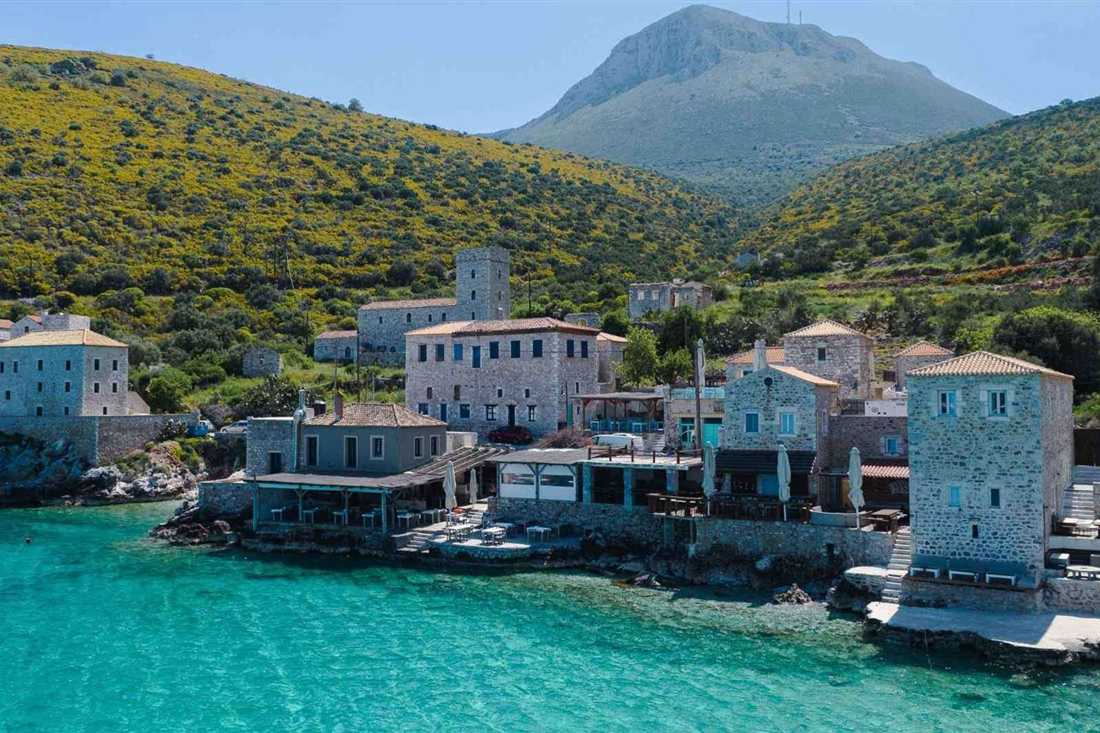Stone tower houses and waterside tavernas on a turquoise bay below a rocky mountain on the Mani coast