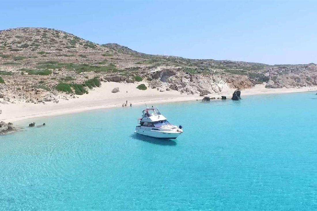White motor yacht anchored in a turquoise bay below a sandy beach and dry hills