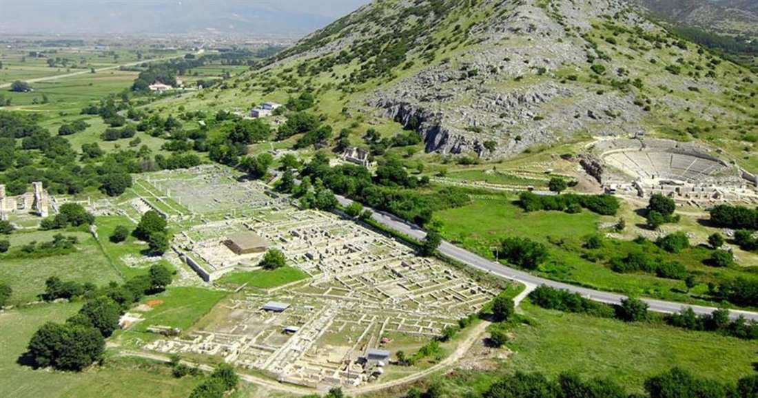 The ruins of ancient Philippi spread across a green plain below a hill, with the theatre on the right, seen from above on a Kavala private tour.