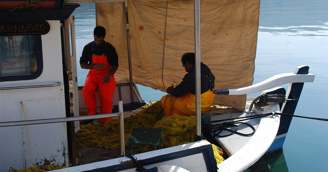 Two fishermen sorting nets on the deck of a small fishing boat in Argostoli harbour, Kefalonia.