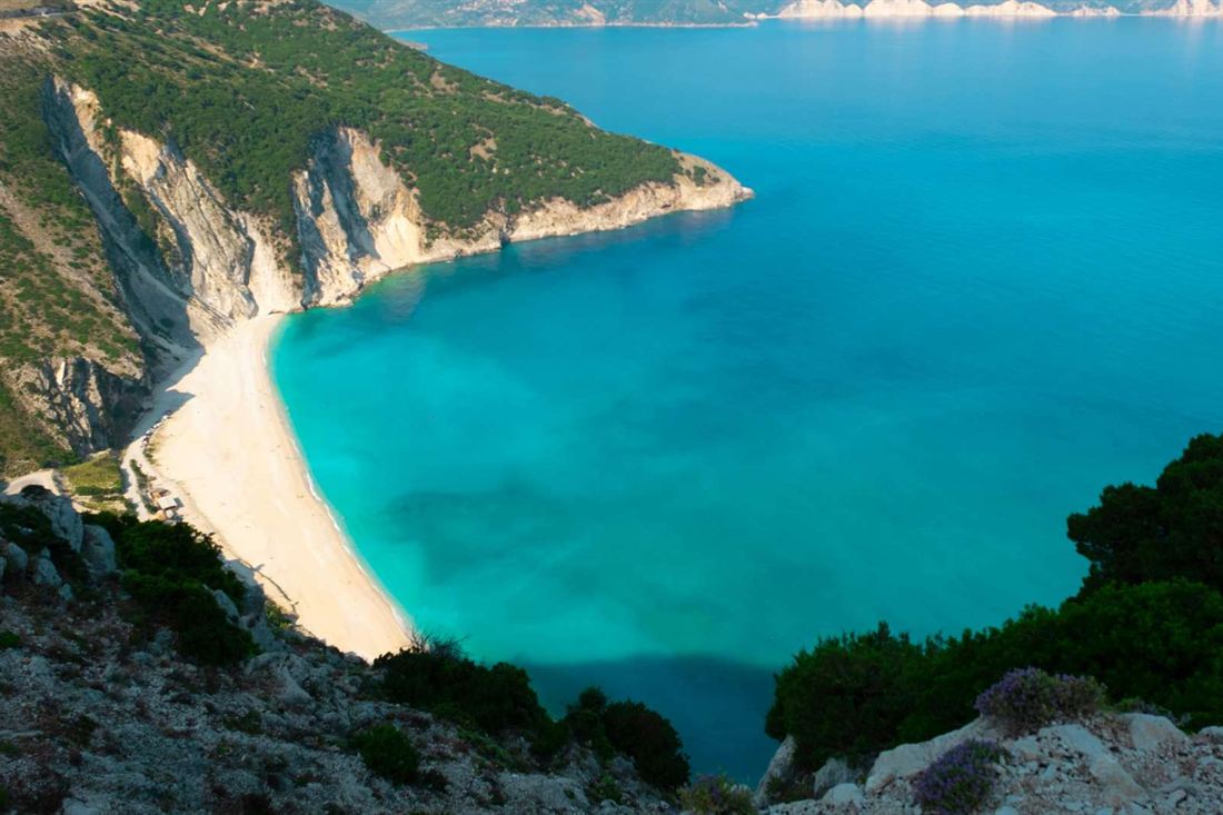 Myrtos beach on Kefalonia seen from the clifftop, a white crescent of pebbles below steep cliffs beside turquoise water