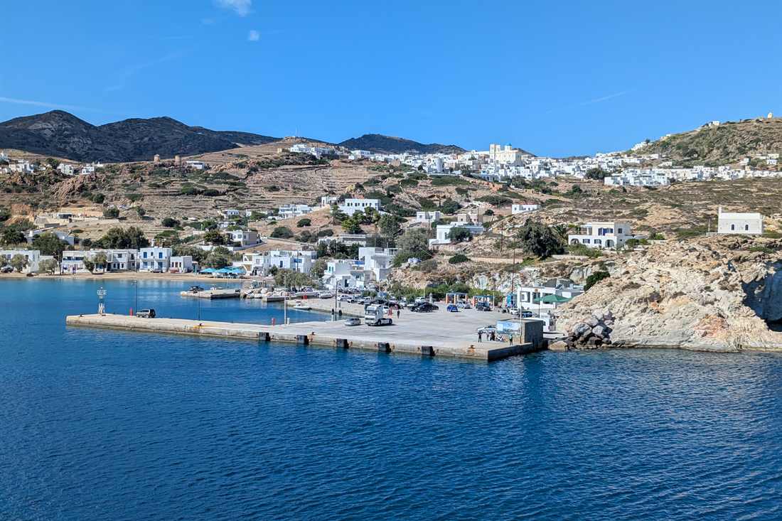 Concrete pier at Psathi harbour on Kimolos with parked cars, white houses on the hillside and deep blue water in front