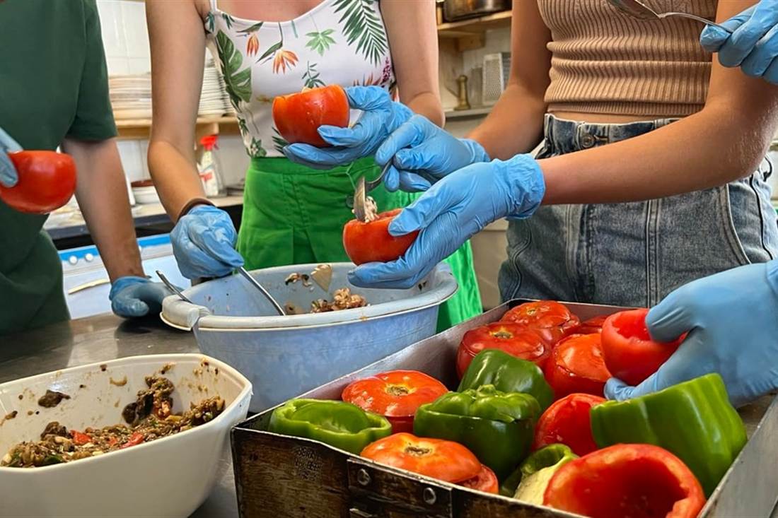 Gloved hands stuffing tomatoes and peppers with a rice filling in a kitchen at a Kos cooking class.