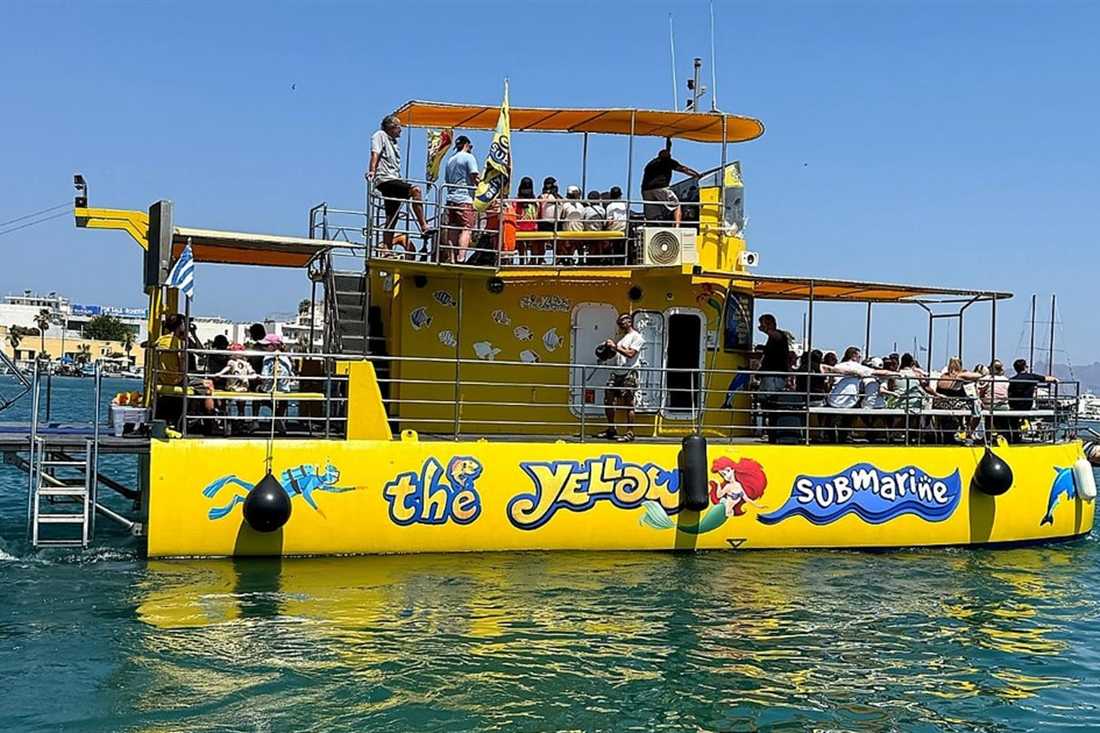 The Yellow Submarine glass bottom boat with guests on its upper deck in clear water off Kos, on a Kos glass bottom boat cruise.