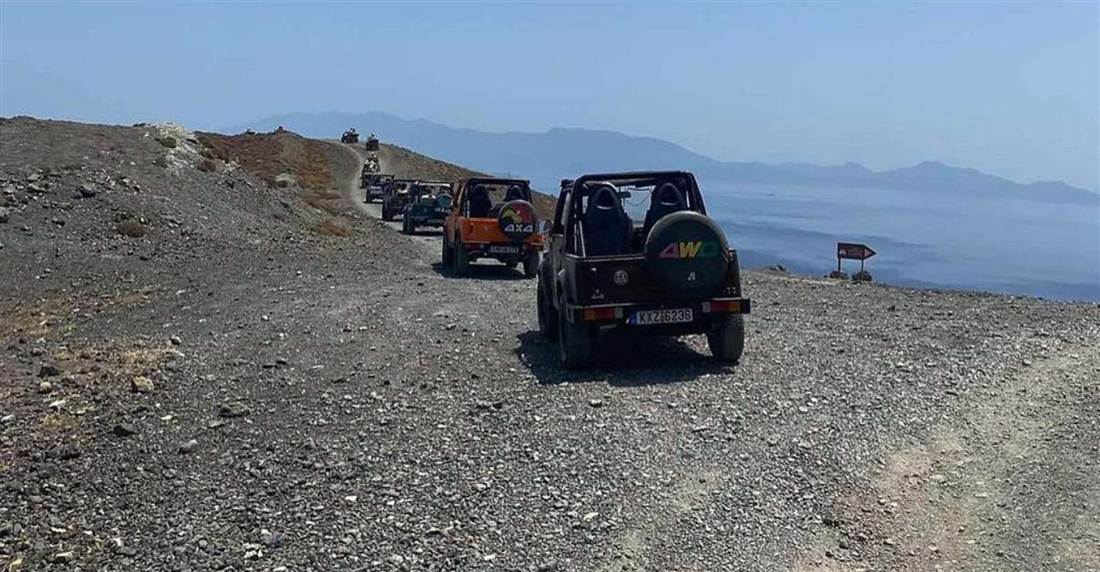 A convoy of open 4x4 vehicles on a gravel track above the sea on Kos, with islands on the horizon