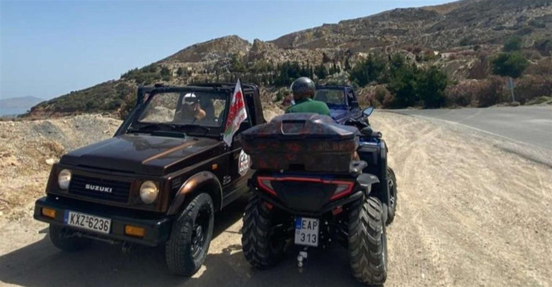 A rider on a quad bike beside an open 4x4 on a dirt road below the hills of Kos