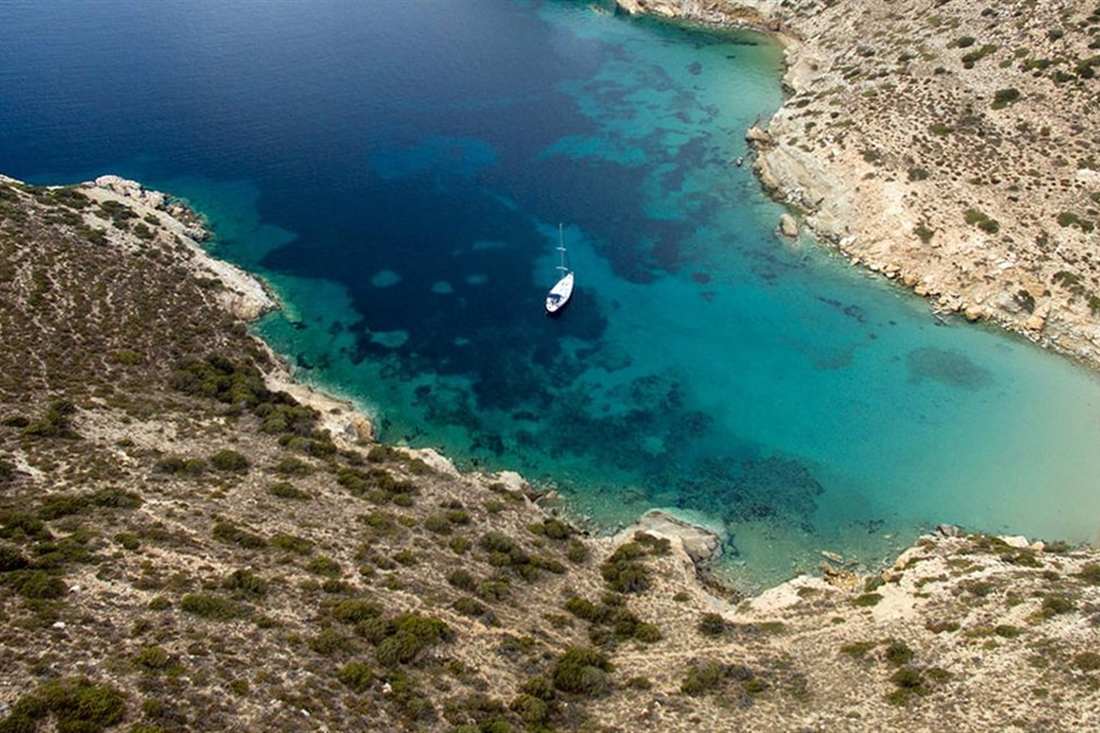 An aerial view of a sheltered cove with clear blue water, a white sand beach and a small boat on Koufonisia.