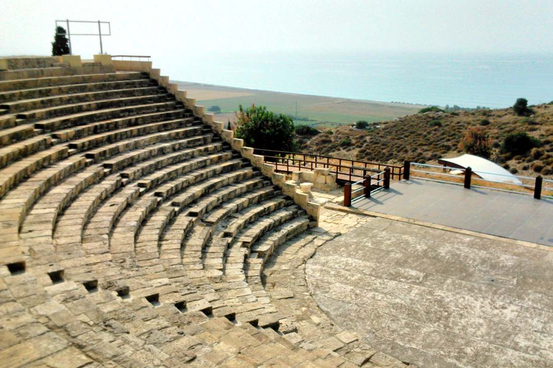 Curved rows of stone seating in the Kourion theatre with the sea and coastal plain behind