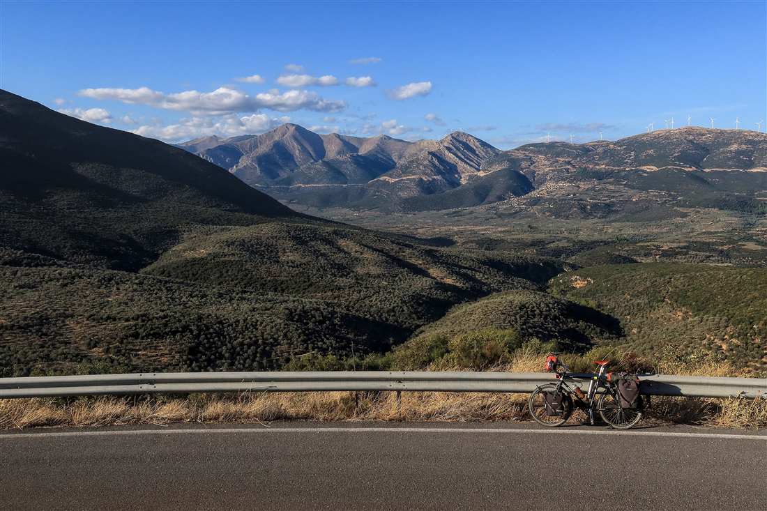 A touring bicycle resting on a mountain road above olive valleys in Greece, the kind of climb a Lefkada e-bike tour rides.