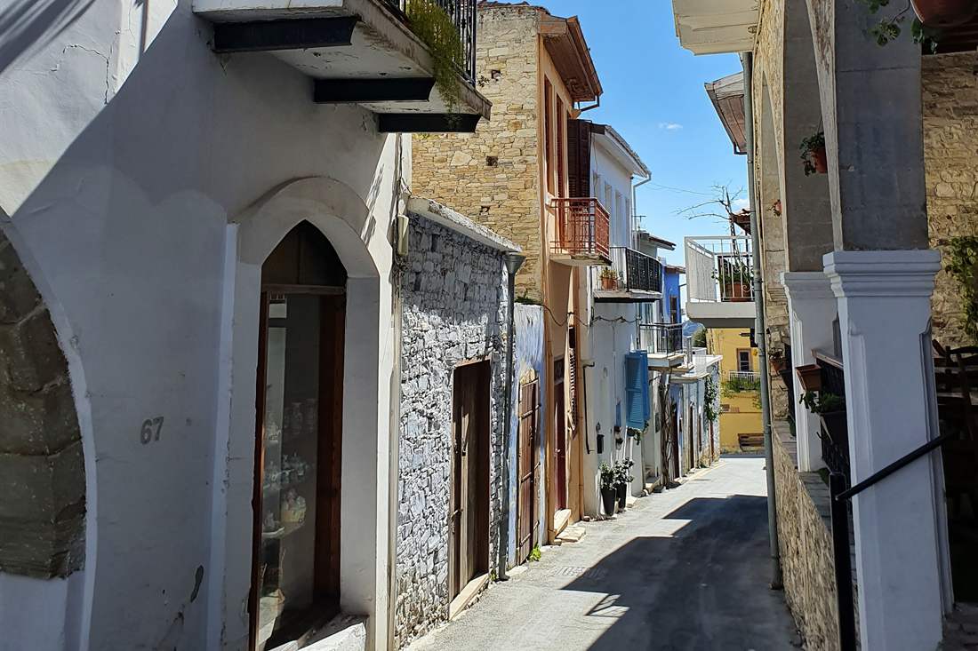 Narrow village lane in Pano Lefkara with white and stone houses, balconies, an arched shop window and a blue sky