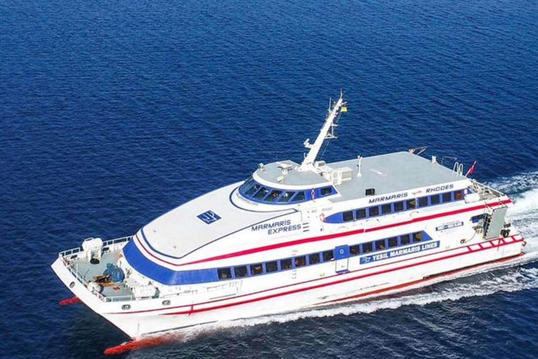 White and blue fast passenger catamaran with red stripes crossing deep blue sea
