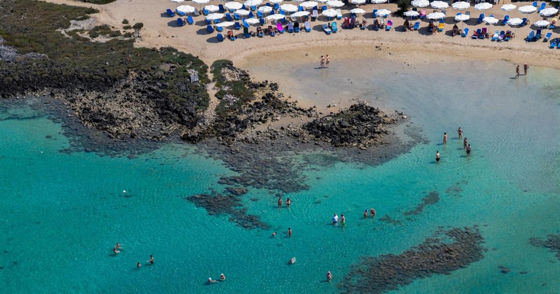 Swimmers in clear shallow water off a beach with sun umbrellas, a swim stop on a Lichadonisia boat trip.