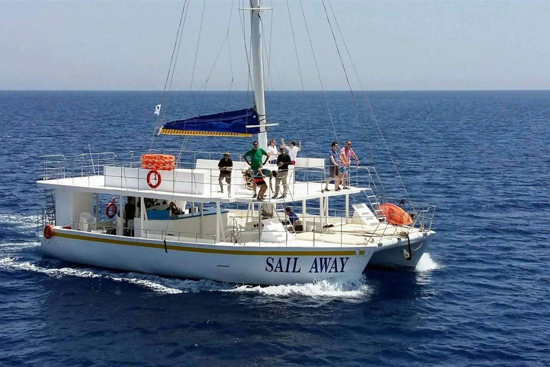Catamaran Sail Away sailing on dark blue open sea with passengers standing on the upper deck