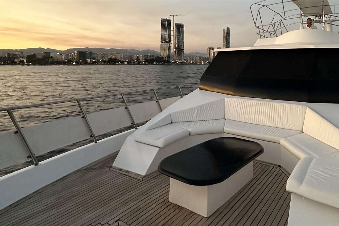 Sunset sky glowing over the Limassol seafront towers, seen from the white lounge seating on the bow deck of a motor yacht