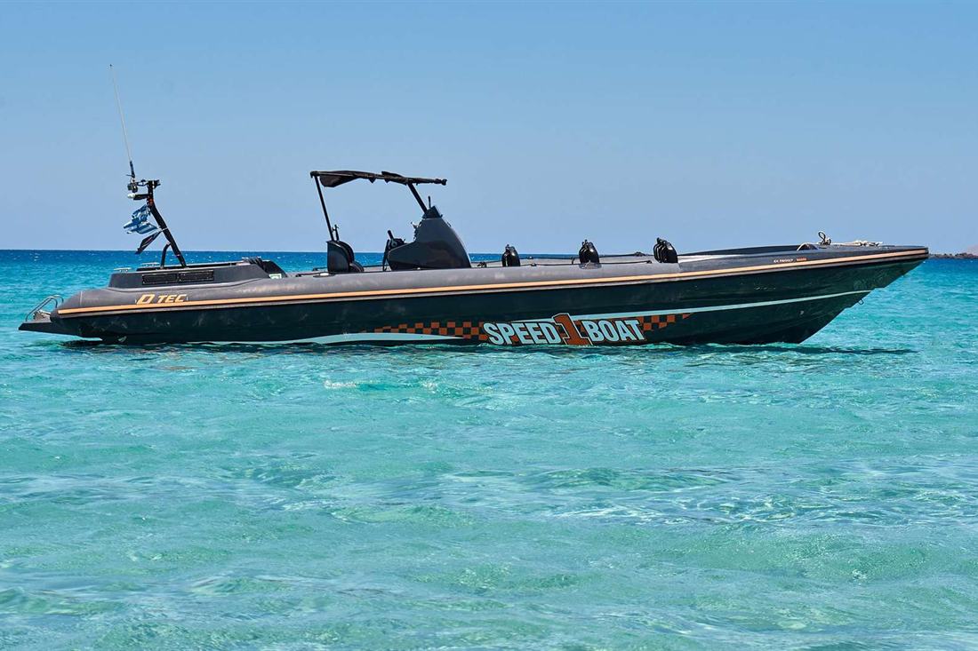 A black speedboat with the words Speed Boat on its side floating on clear turquoise water under a blue sky.