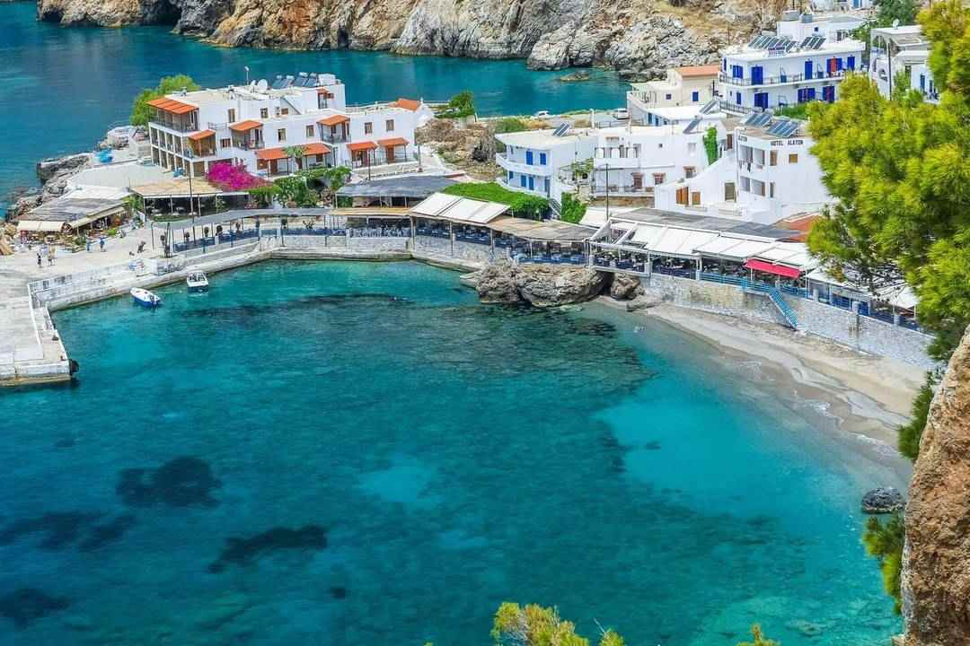 The white houses and waterfront tavernas of Loutro around a turquoise bay, with a small pebble beach and rocky slopes.