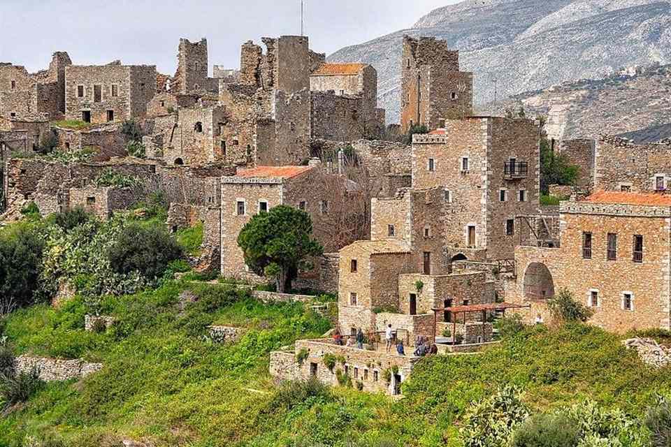 The stone tower houses of Vathia in the Mani, rising on a green hillside below a bare grey mountain.