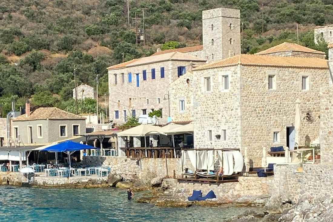 Stone tower houses and a waterfront taverna at Limeni bay in the Mani, above clear blue-green water.
