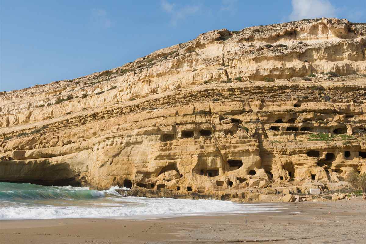 Matala beach under the sandstone cliff with its rock-cut caves on the south coast of Crete, the goal of a Matala day trip from Heraklion