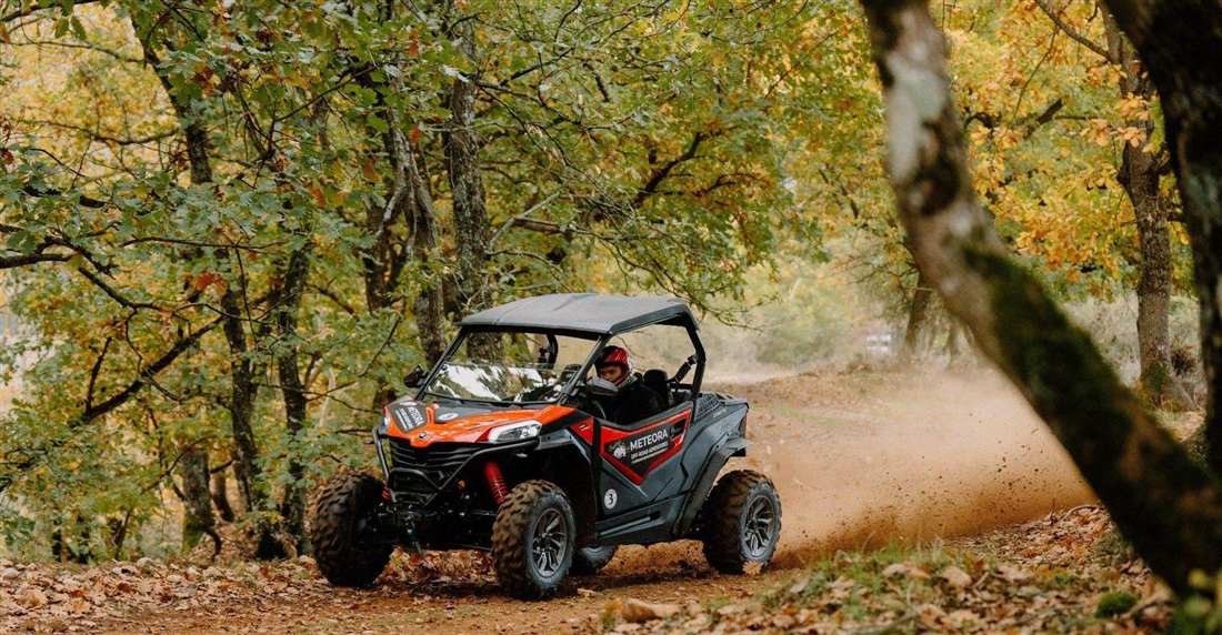 An off-road buggy kicking up dust on a dirt track through autumn oak woods near Meteora