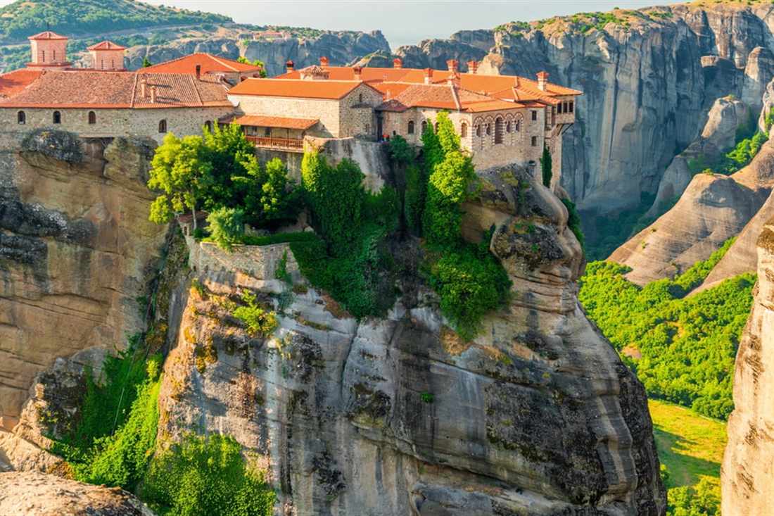 A monastery with red-tiled roofs on top of a sheer rock pillar among the cliffs of Meteora, seen on a Meteora private tour.