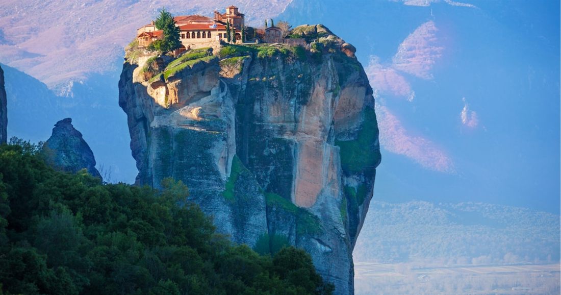 A monastery perched on the summit of a lone rock tower at Meteora, with green trees below, on a Meteora private tour.