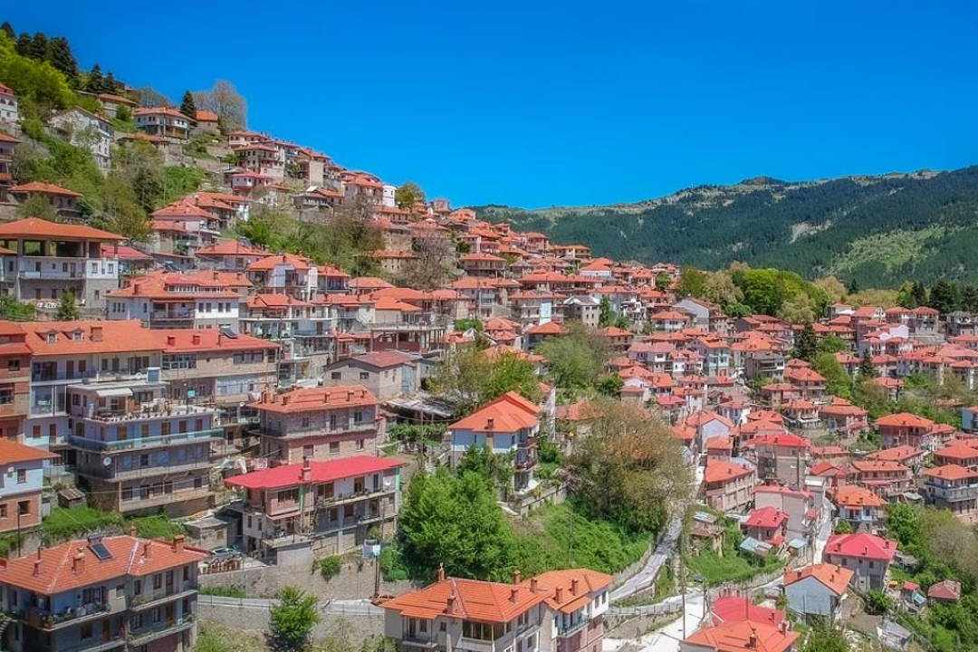 Metsovo spread across a green mountainside in the Pindus, with rows of red-roofed stone houses under a blue sky.