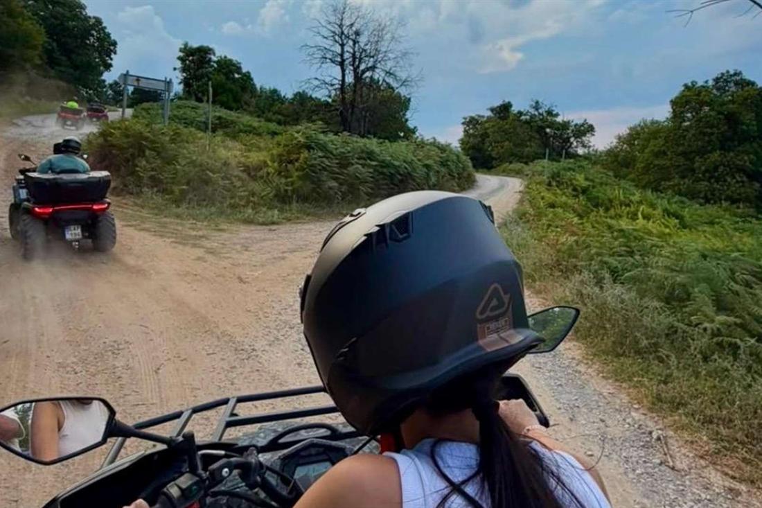 A rider in a helmet follows a quad bike along a dirt forest track on an ATV tour