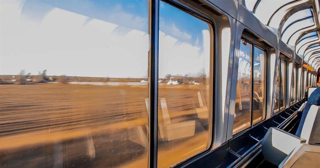 Inside a train carriage with wide windows and fields rushing past, on the rail journey of a Mount Olympus day trip from Athens.