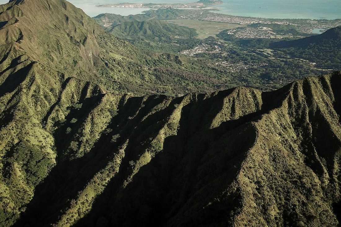 Rugged ridges and deep ravines of Mount Olympus seen from above, with the plain and the sea in the distance.