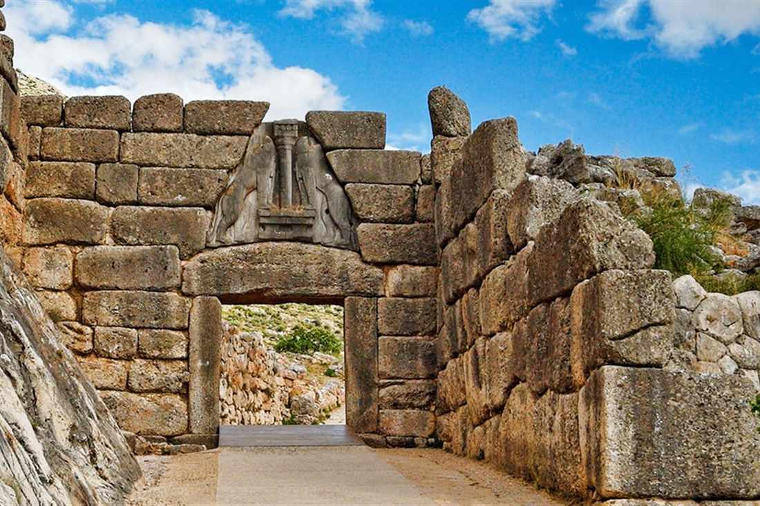 The Lion Gate of Mycenae, with two carved lions above the lintel, set in walls of huge stone blocks under a blue sky.