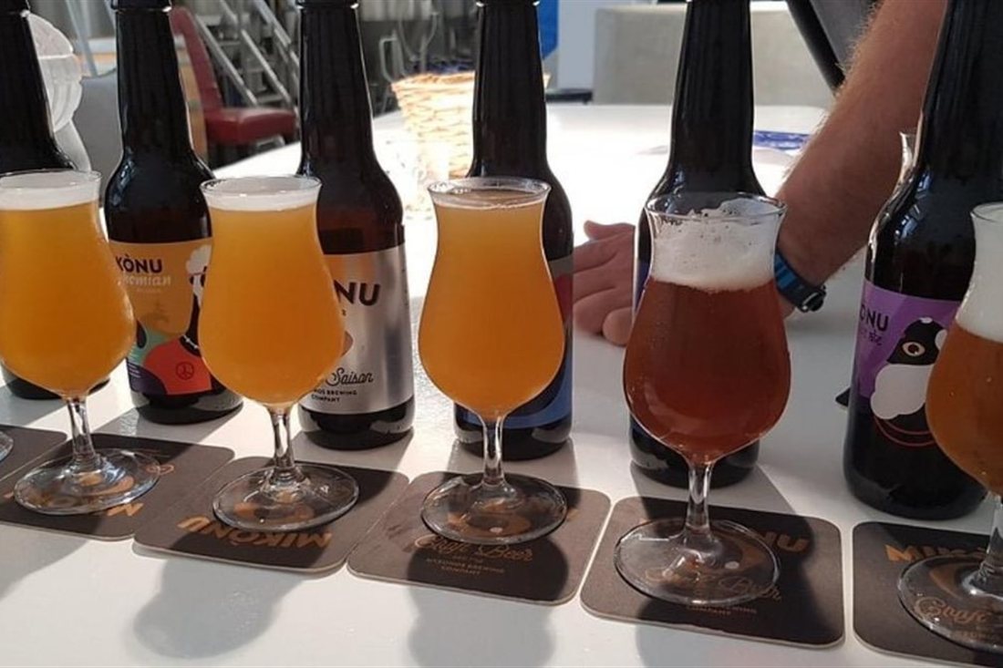A row of tasting glasses of golden and amber Mikonu craft beer beside their bottles on a table, at a Mykonos beer tasting.
