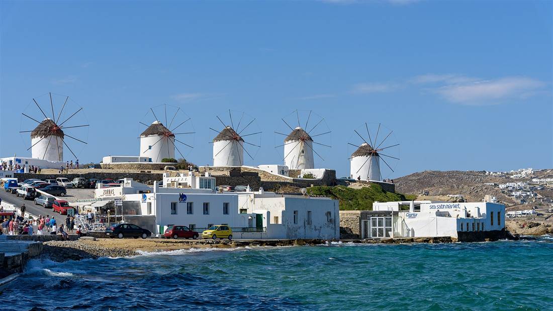 The white windmills of Kato Mili on the ridge above the sea and the edge of Mykonos Town, a stop at the end of a Mykonos bus tour.