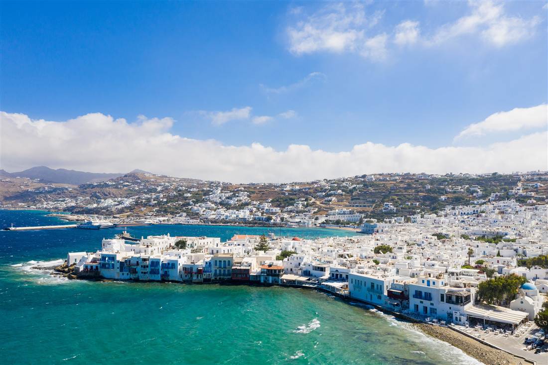 Little Venice and the white houses of Mykonos Town on the shore, with the ferry and cruise terminal across the bay, seen on a Mykonos shore excursion.
