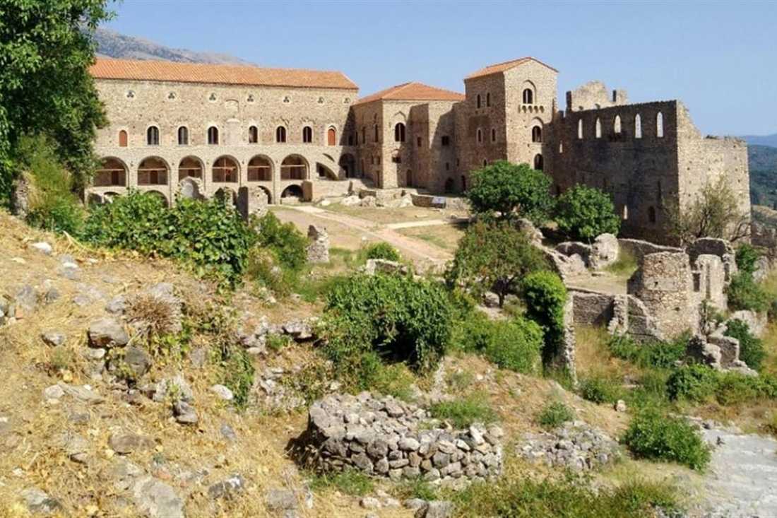 The restored Palace of the Despots at Mystras, a long stone building with arched windows, above a green slope of ruins.