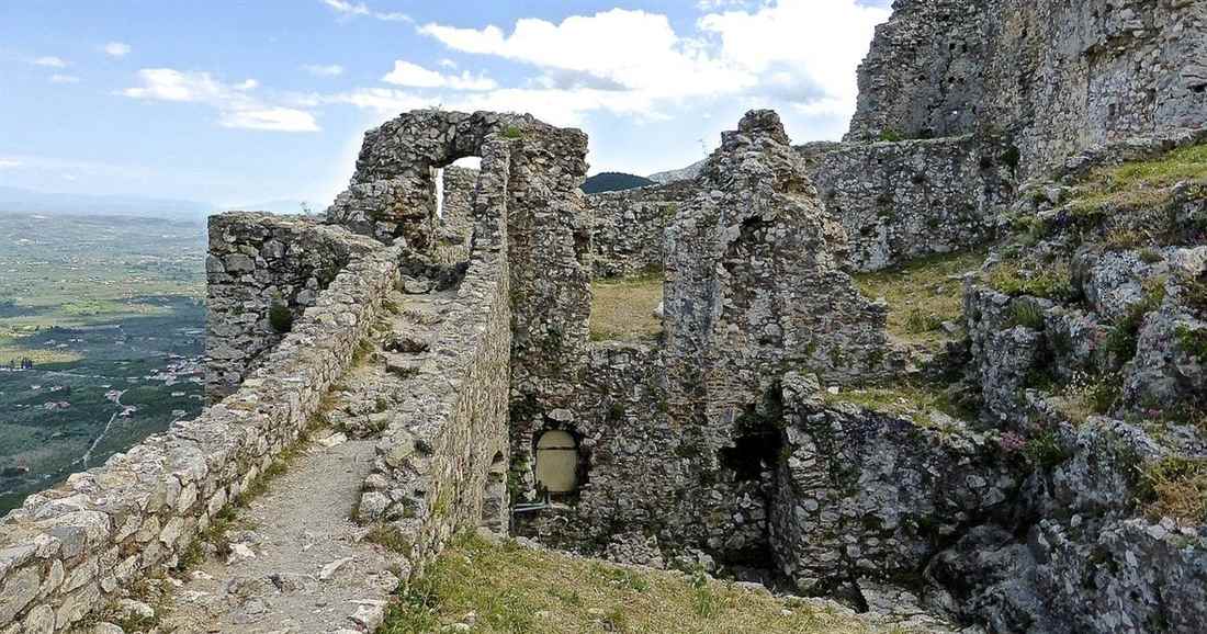 Stone walls and a narrow path inside the ruined castle above Mystras, with the green plain of the Evrotas valley below.