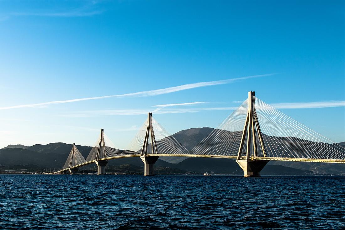 The Rio-Antirrio bridge with its cable-stayed pylons crossing the dark blue Gulf of Corinth under a clear blue sky.