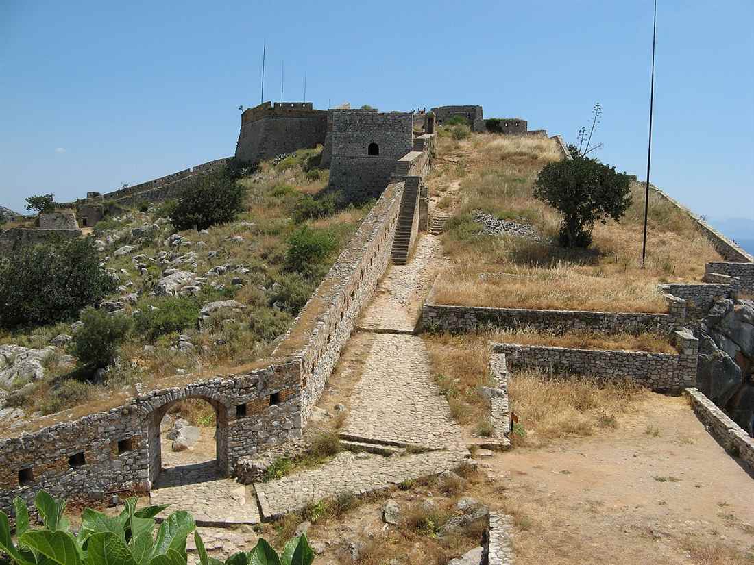 The stone walls and paved path of Palamidi fortress climbing a dry hill above Nafplio.