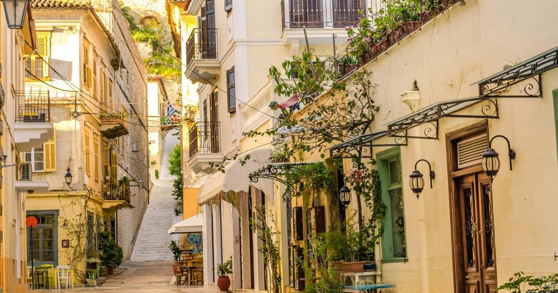 A narrow lane of the old town of Nafplio with stairs, balconies and flowers, a short walk from a Nafplio hop on hop off stop.