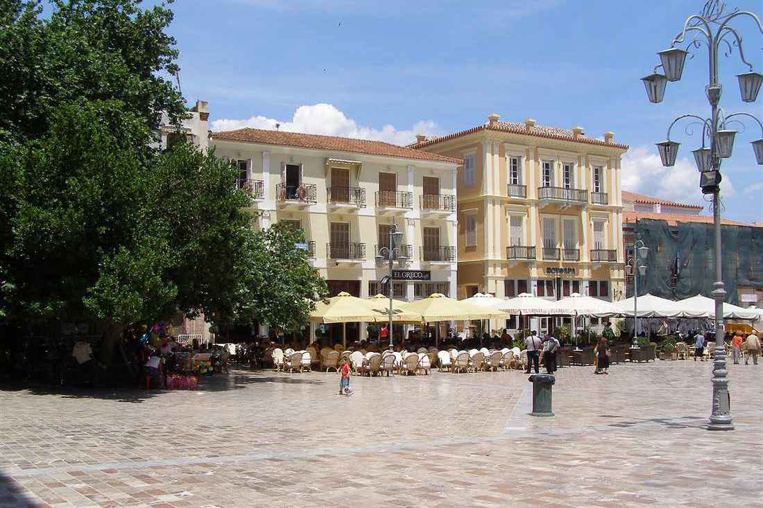 Syntagma Square in the old town of Nafplio, with neoclassical buildings and cafe tables under a blue sky